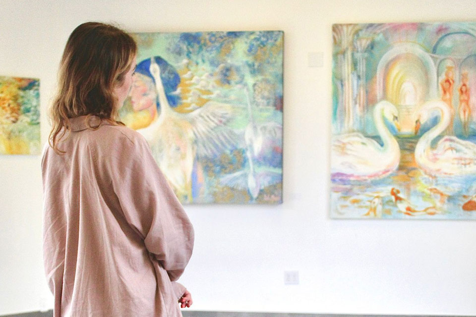 Woman viewing ethereal swan-themed paintings in a softly lit gallery space, immersed in a serene and dreamlike art exhibition.