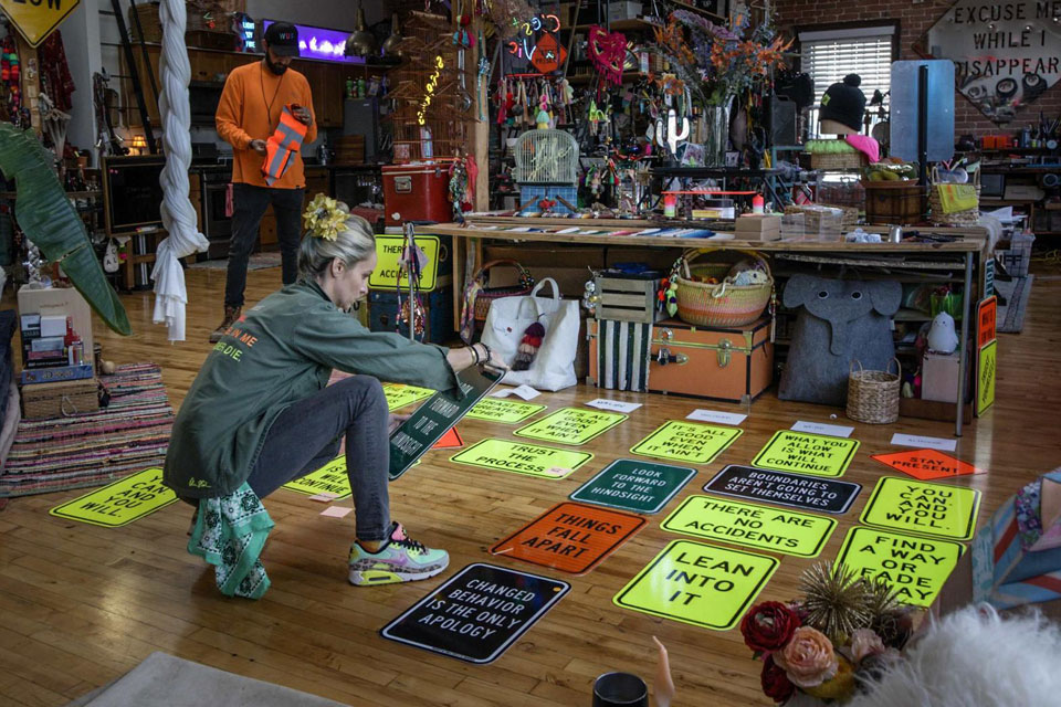 Olivia Steele arranging her signature neon oracle signs in a vibrant studio filled with symbolic art, affirmations, and creative tools.