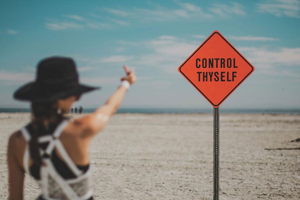 Woman pointing at a desert art installation sign that reads “CONTROL THYSELF” by Olivia Steele.