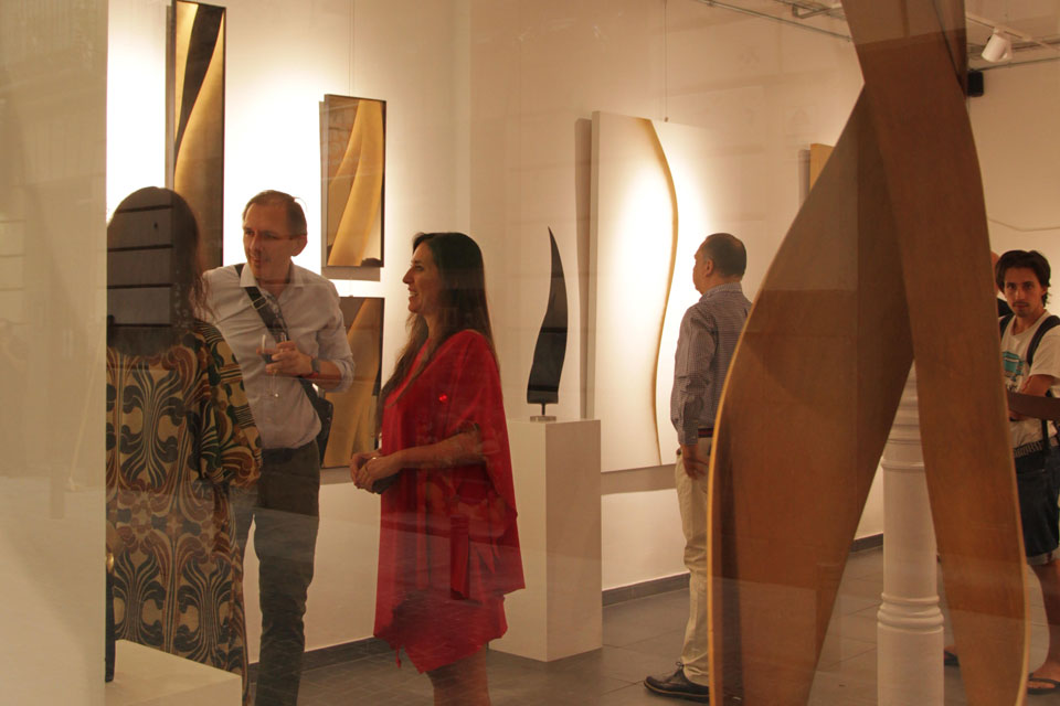 Visitors interact and observe sculptural works at Veronica Mar’s gallery exhibition featuring abstract, flowing forms in a minimalist space.